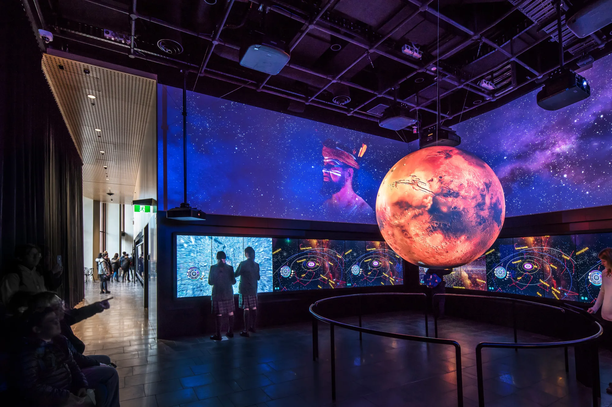 Inside Uni SA Cancer Research Institute darkly lit room with multiple screens on each wall and a hanging moon on display in the centre