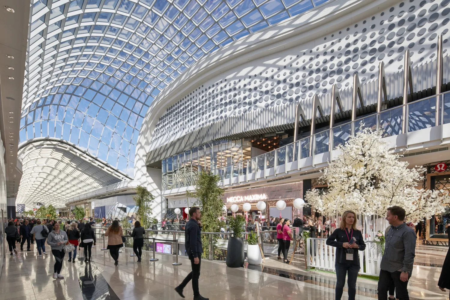 Interior view of walkway with curved glass roofing above.