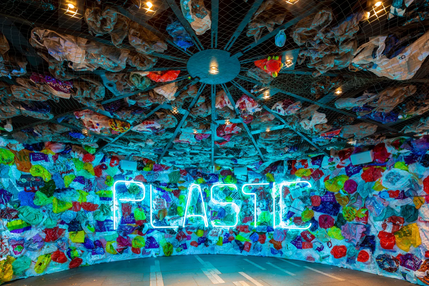 Central neon lights spelling the word 'Plastic' surrounded by plastic carrier bags