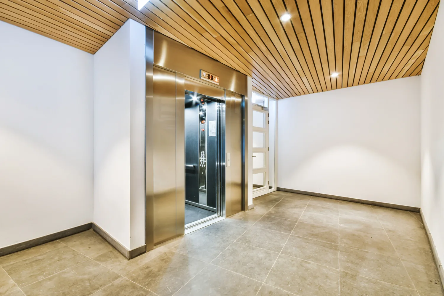 Lift area with wooden ceiling and stone flooring with one lift with door open