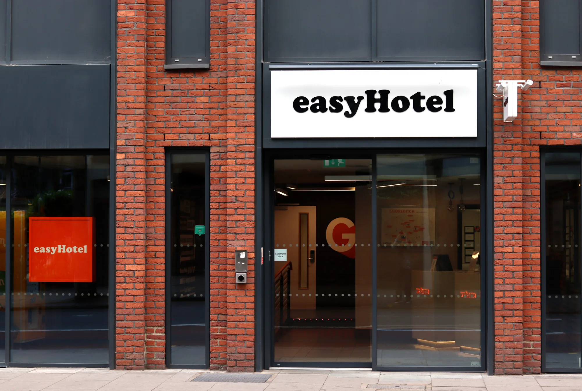 Open front glass door of easyHotel with a red brick facade.