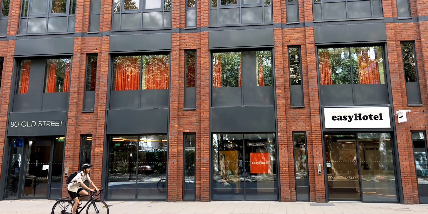 Red brick exterior of easyHotel with large glass windows. White sign with black text saying 'easyHotel'.