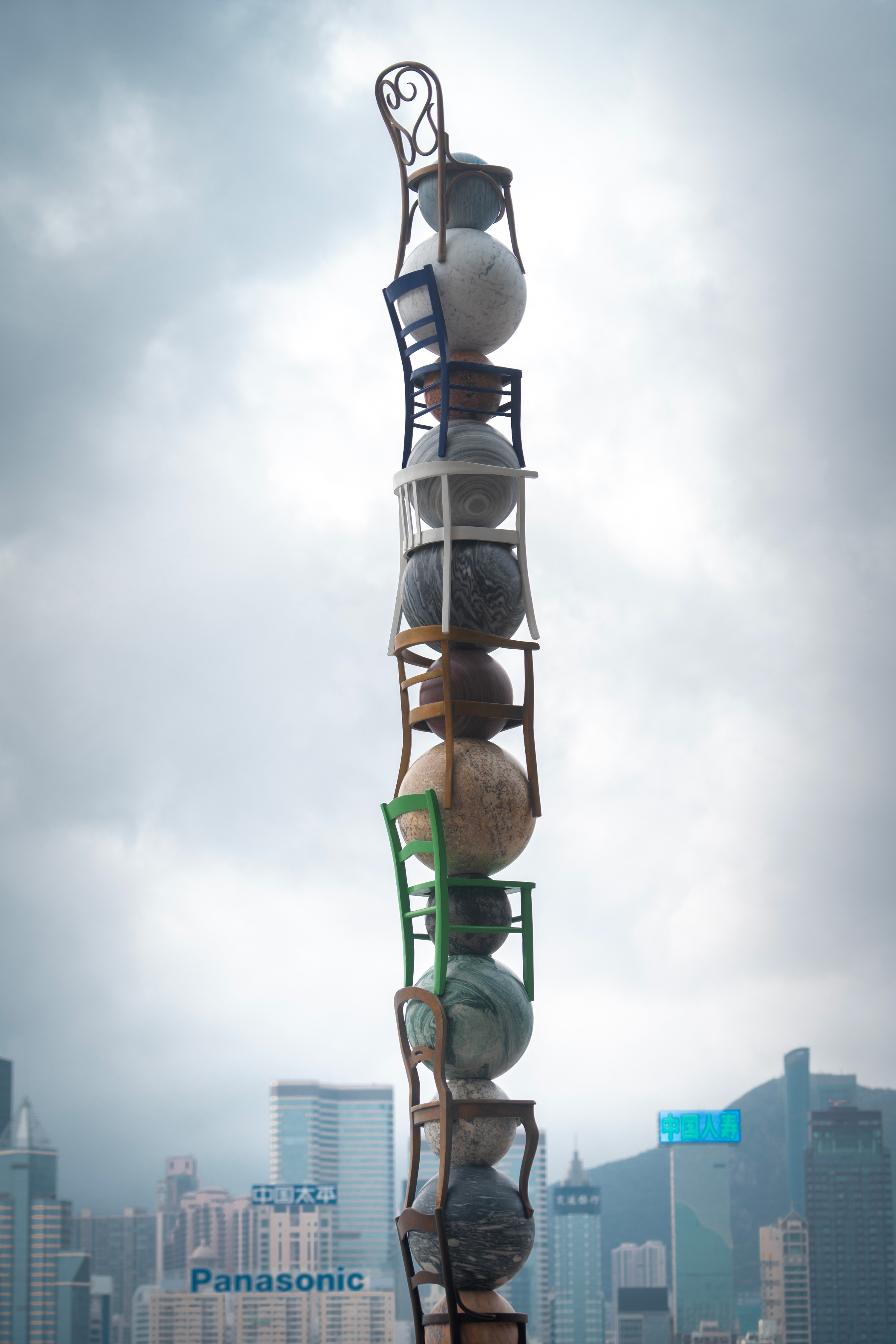 The artwork features seven marble spheres representing planets, suspended above a framework made of ordinary chairs.