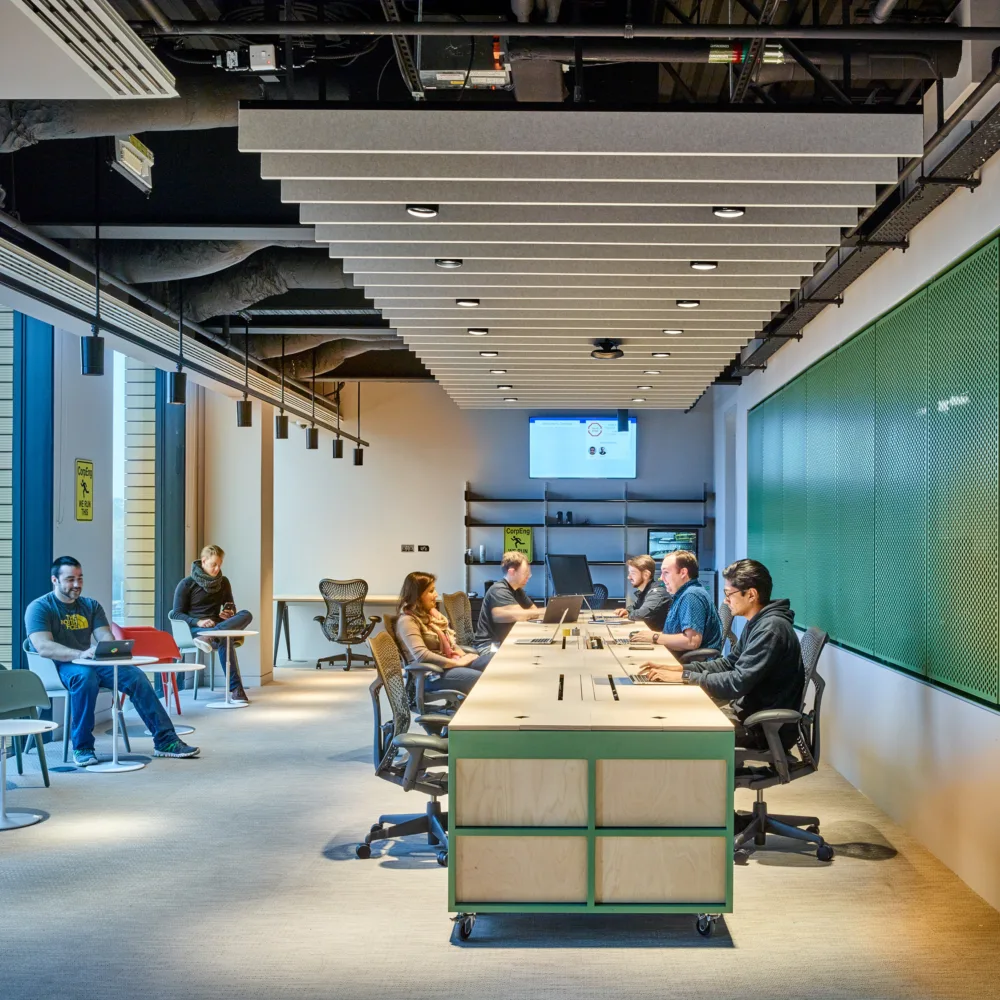 People hotdesking on one large desk and small individual desks at Google offices in 6 Pancras Square