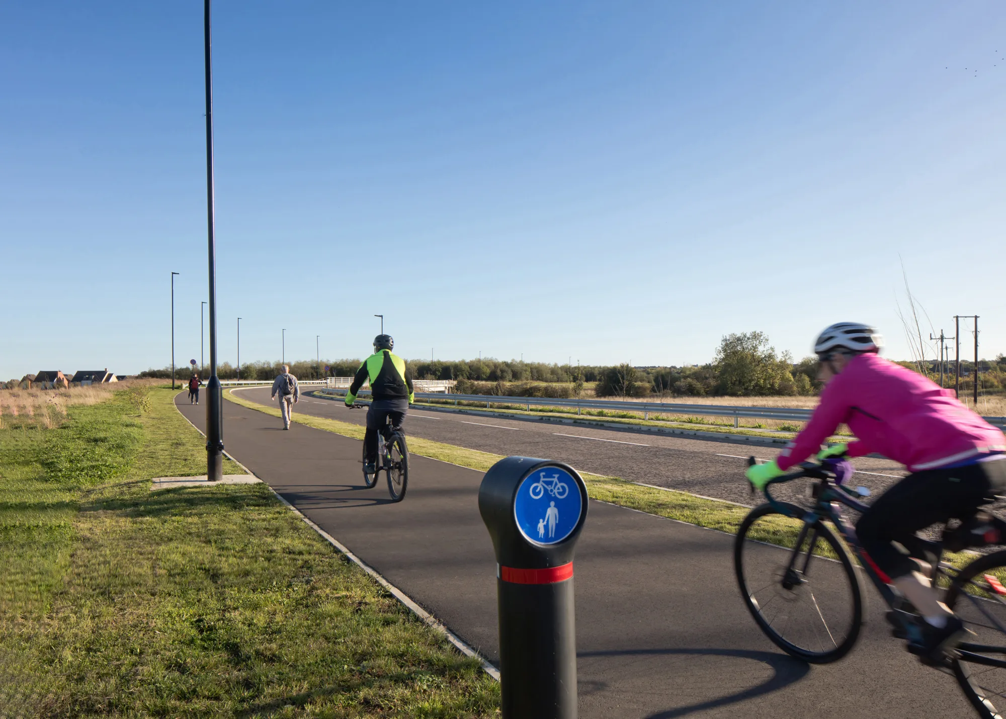 2 cyclist wearing high vis on cycle lane on a bright day with blue sky