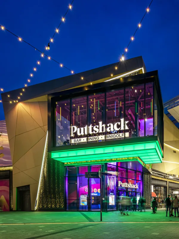 Exterior entrance to Intu Lakeside shopping centre in the evening. With exterior lighting and people shopping