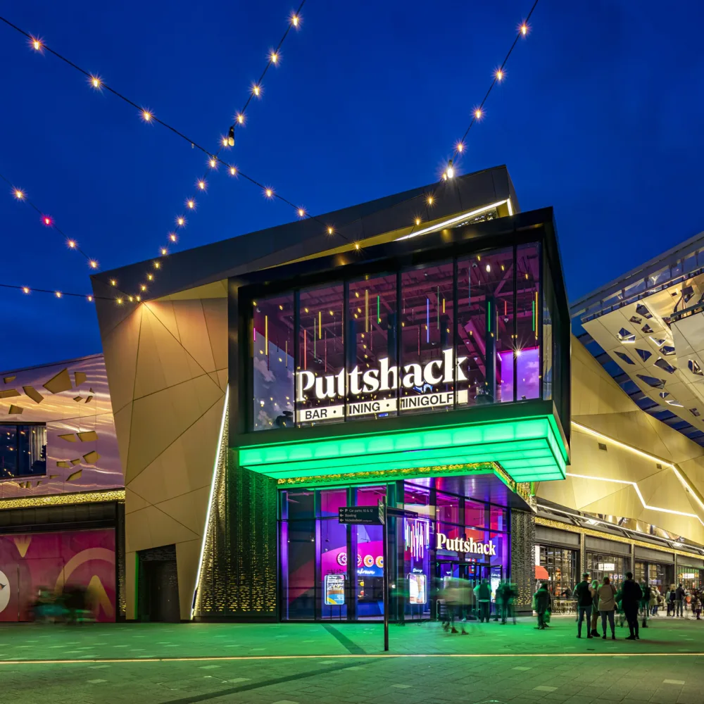 Exterior entrance to Intu Lakeside shopping centre in the evening. With exterior lighting and people shopping