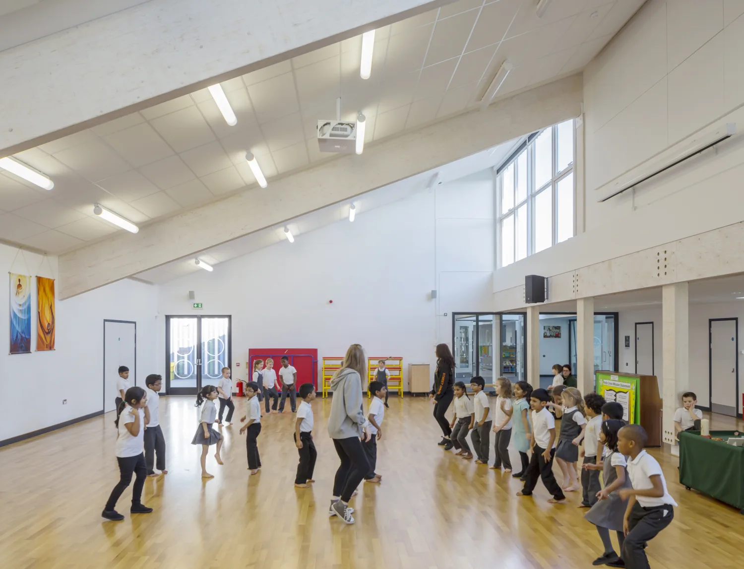 Holy Cross School hall with PE lesson taking place. Wooden flooring with white walls and lighting
