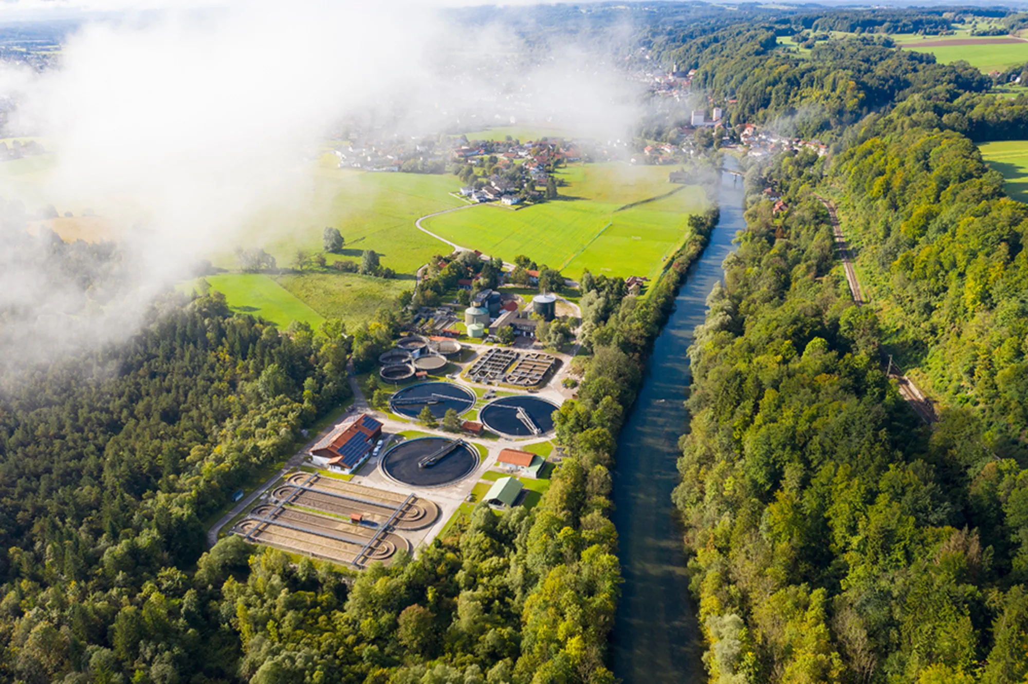 Sewage plant near country village with river and trees with a cloud in the four ground