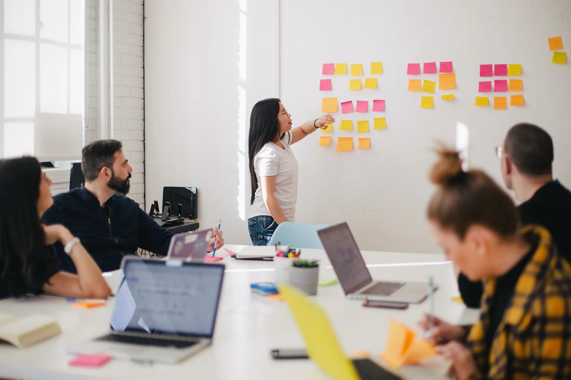 People in meeting with post it notes on board and laptops on table