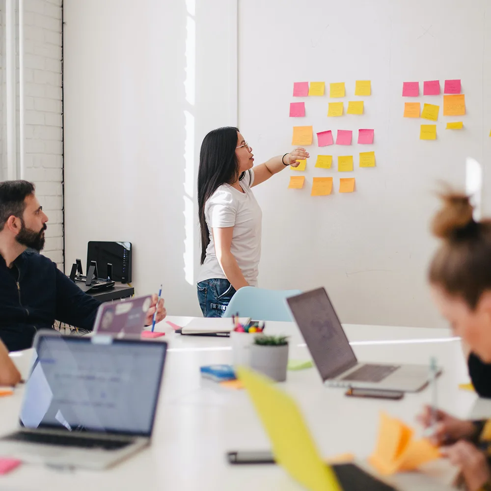 People in meeting with post it notes on board and laptops on table