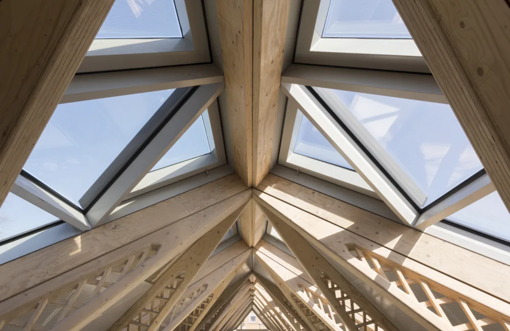 Upward view of a wooden ceiling structure with glazed panels and daylight shining through