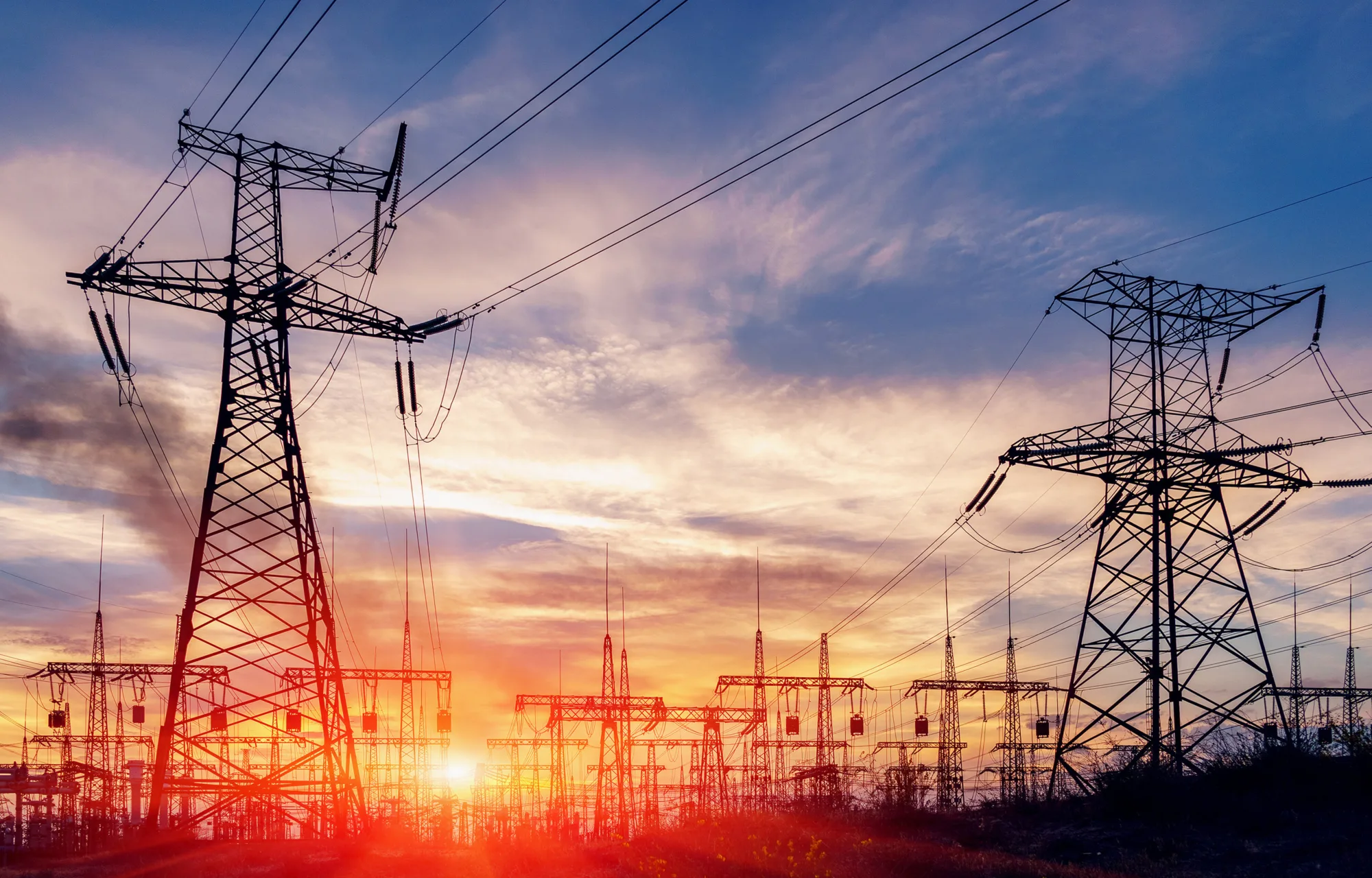 Pylons leading into an electricity plant with the sun setting behind