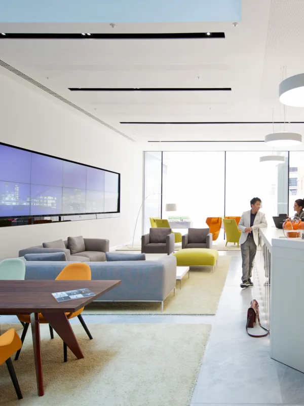 Main office building reception with desks, sofas and a large welcome screen with visitors in the background