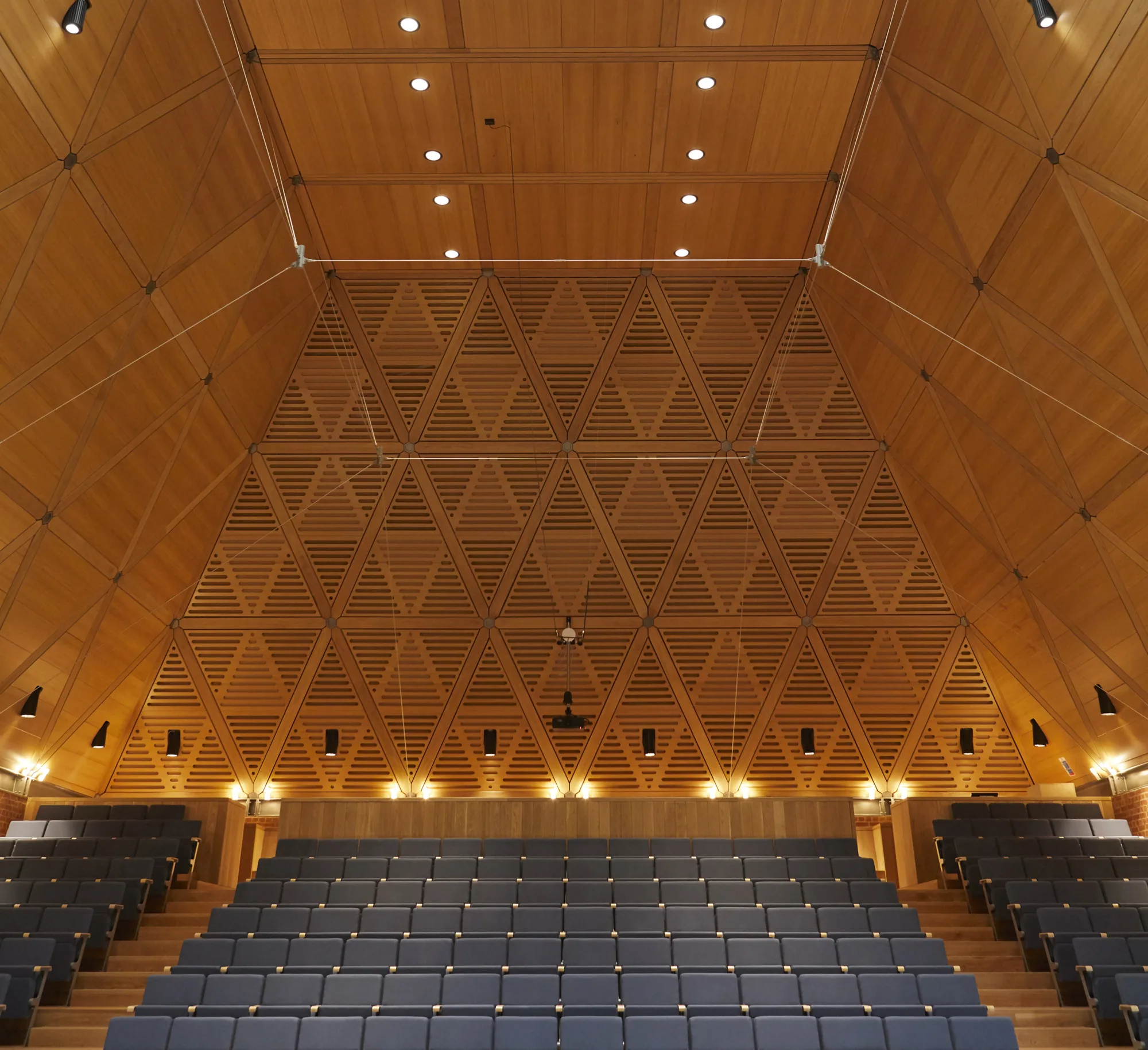 King’s College Music School Wimbledon theatre room with wooden structural panelling and blue seating lit up with warm lighting