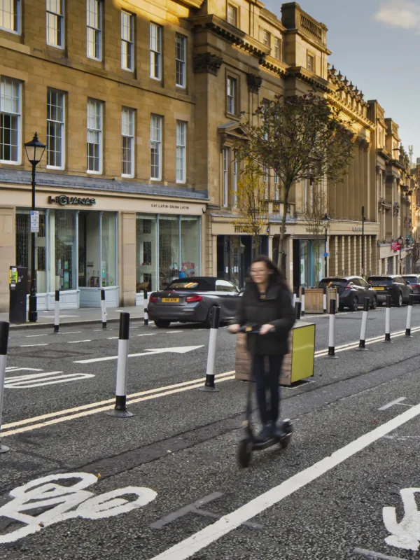 Newcastle street with road signage and lady on a scooter with shops in the background