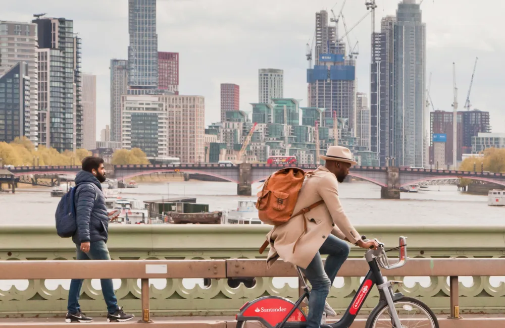 One pedestrian and one cyclist crossing a bridge over the river Thames with high rise buildings under construction in the background