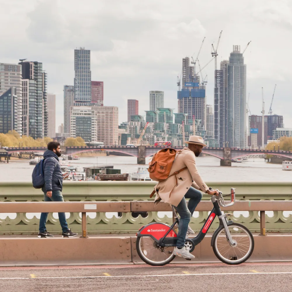 One pedestrian and one cyclist crossing a bridge over the river Thames with high rise buildings under construction in the background