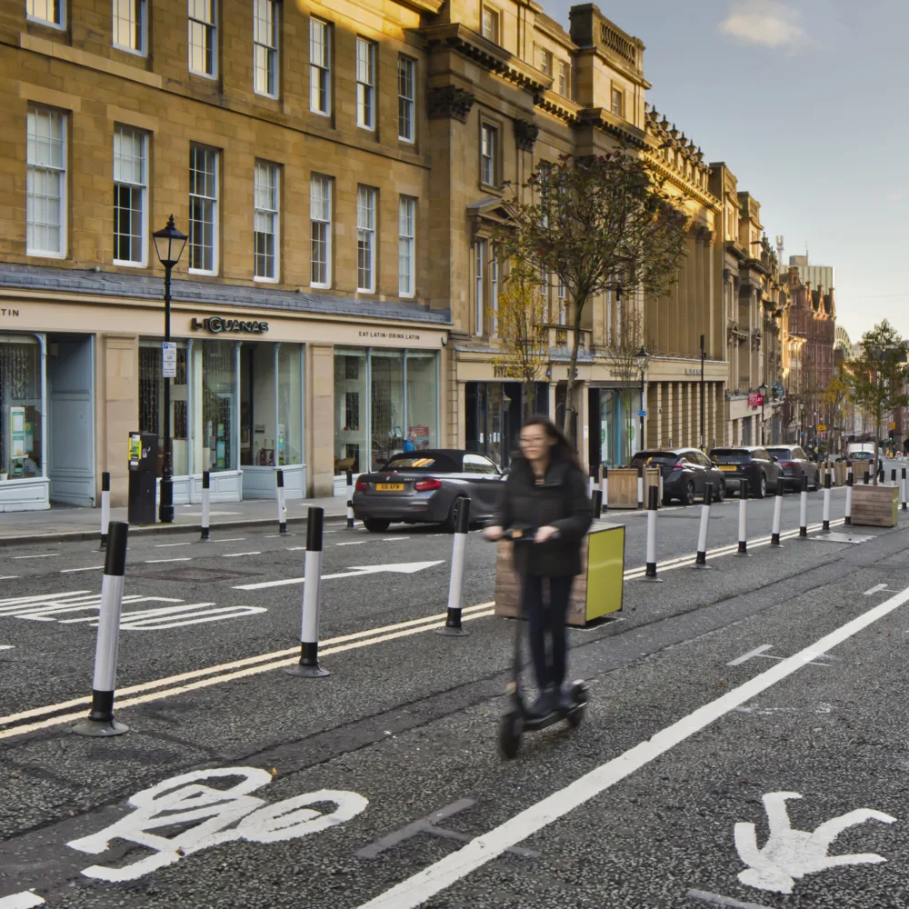 Newcastle street with road signage and lady on a scooter with shops in the background