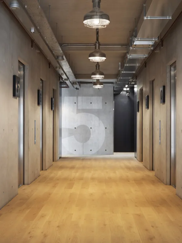 Lift area in an office building with wooden flooring and concrete wall style with level 5 at the end of the corridor