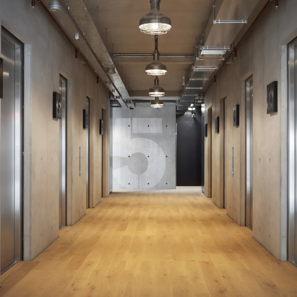 Lift area in an office building with wooden flooring and concrete wall style with level 5 at the end of the corridor