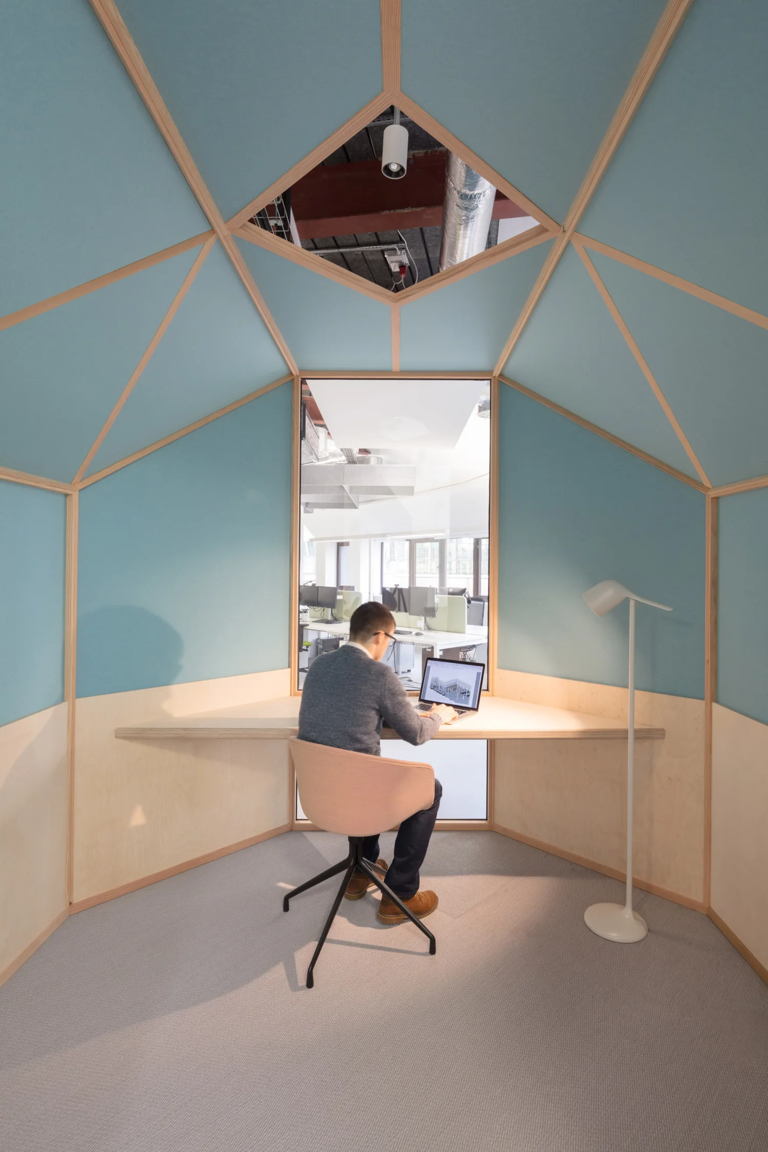 Office acoustic pod with blue panelling and wooden frame and desk with a worker