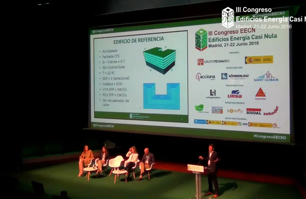 Jose on stage with a panel of seated speakers in front of a large projection screen