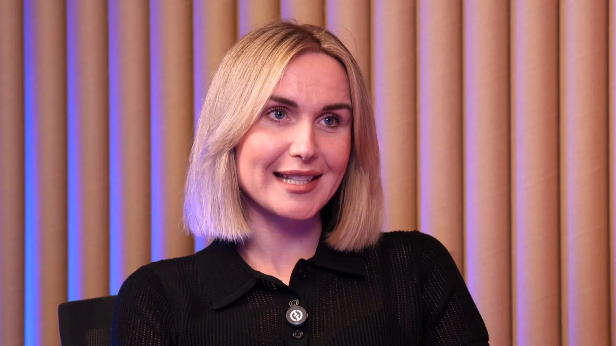Alina Godunova, with blonde hair and black dress, being interviewed and smiling.
