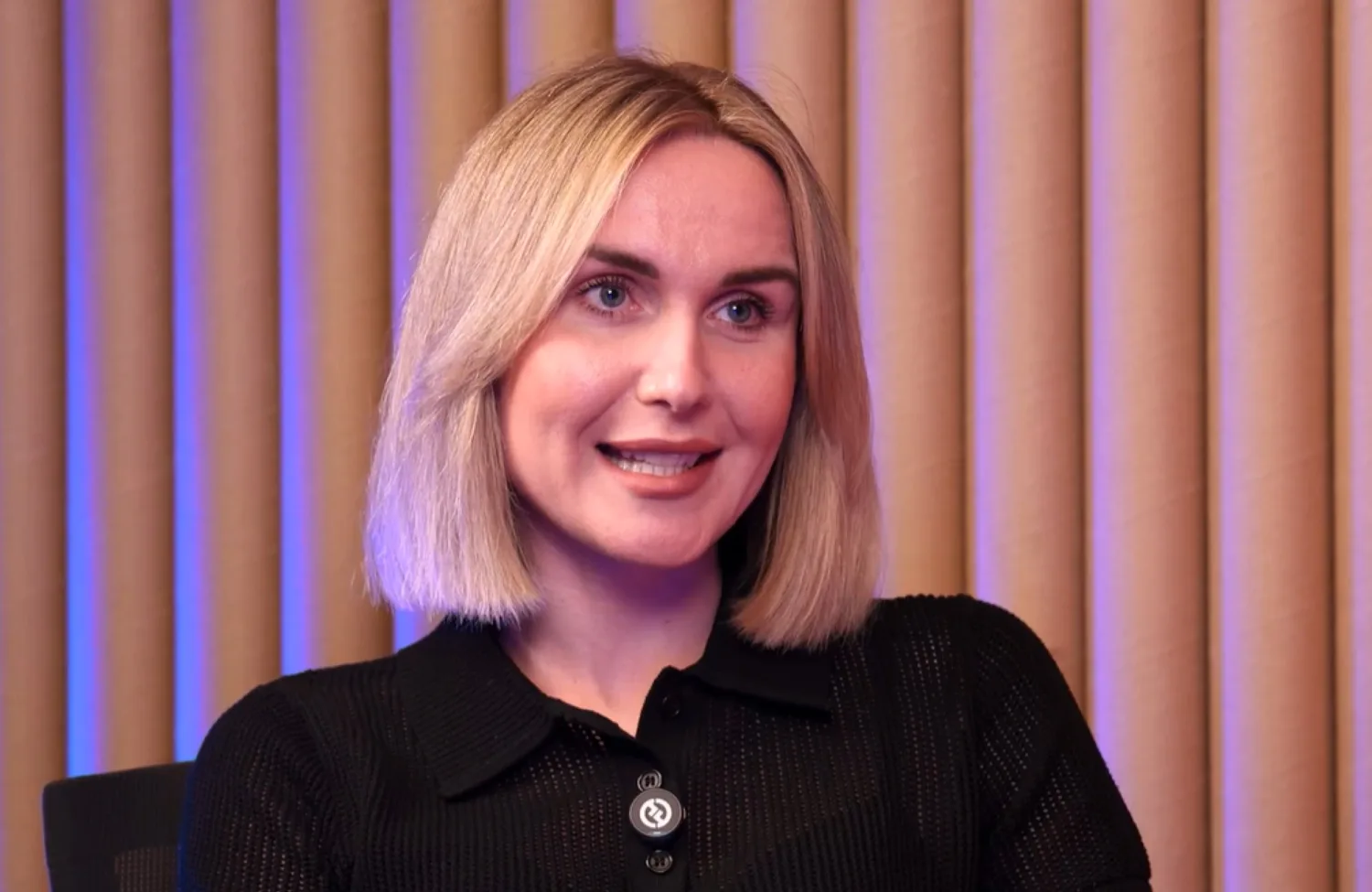 Alina Godunova, with blonde hair and black dress, being interviewed and smiling.
