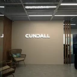 Commercial office interior with illuminated Cundall wall sign, glass partitions, timber slats, seating and ceiling lighting.