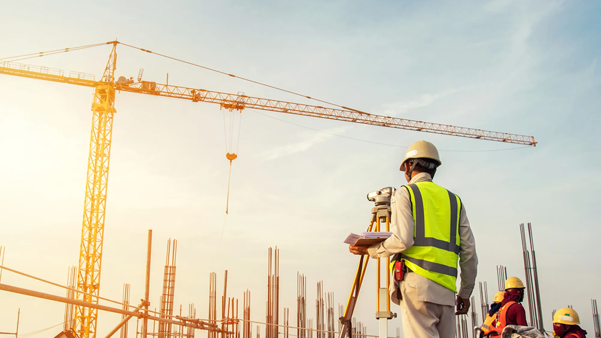 Construction workers on a building site with a yellow crane against a sunlit blue sky