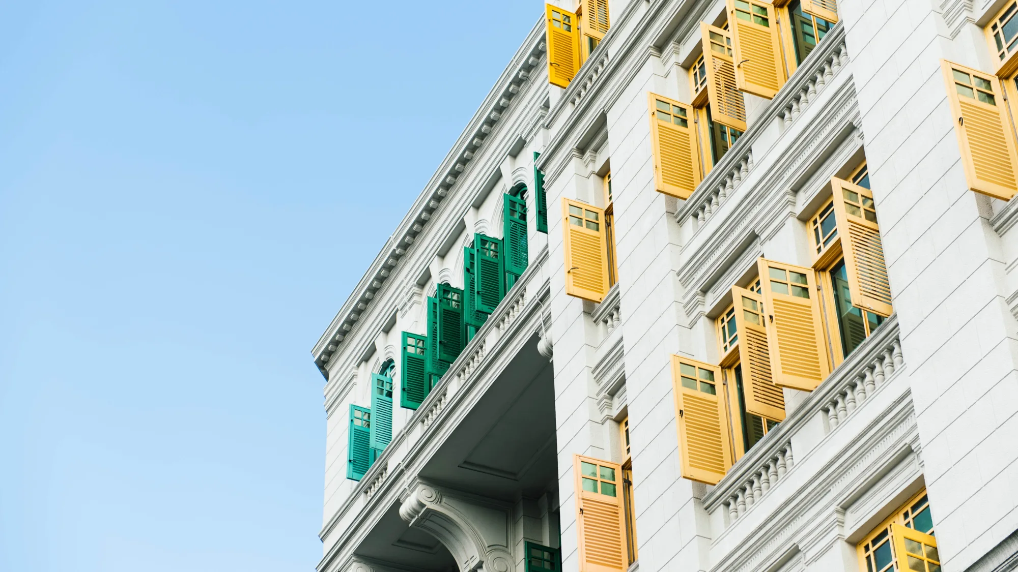 White building with yellow and green shutters against a blue sky