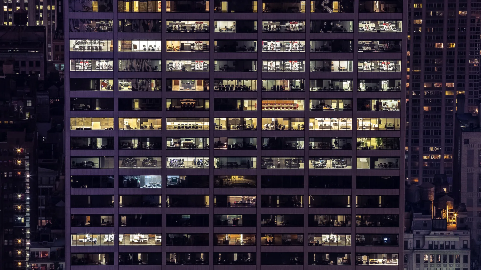 Exterior of an offlice building at night time with lit office spaces and workers