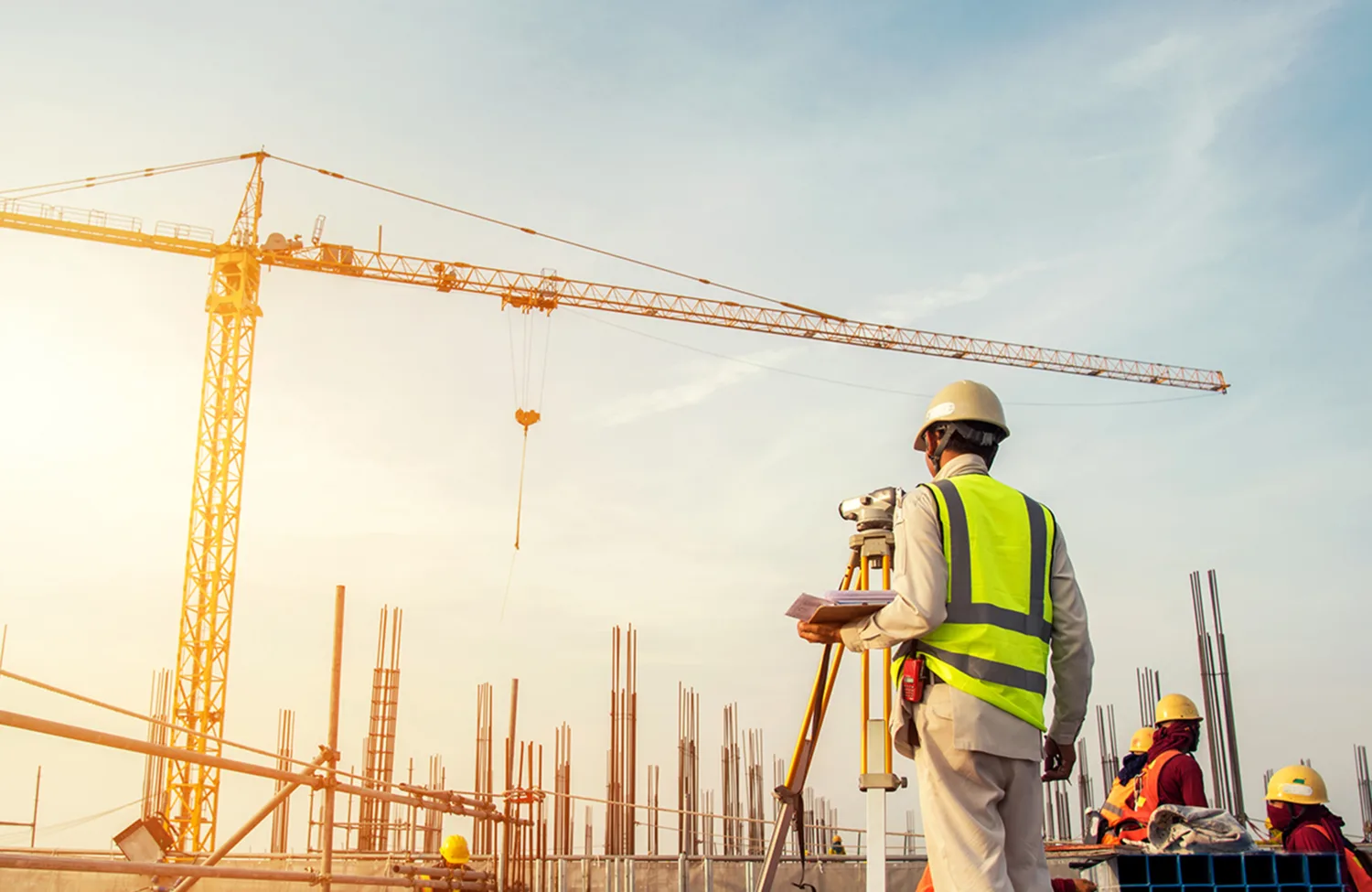 Construction workers on a building site with a yellow crane against a sunlit blue sky