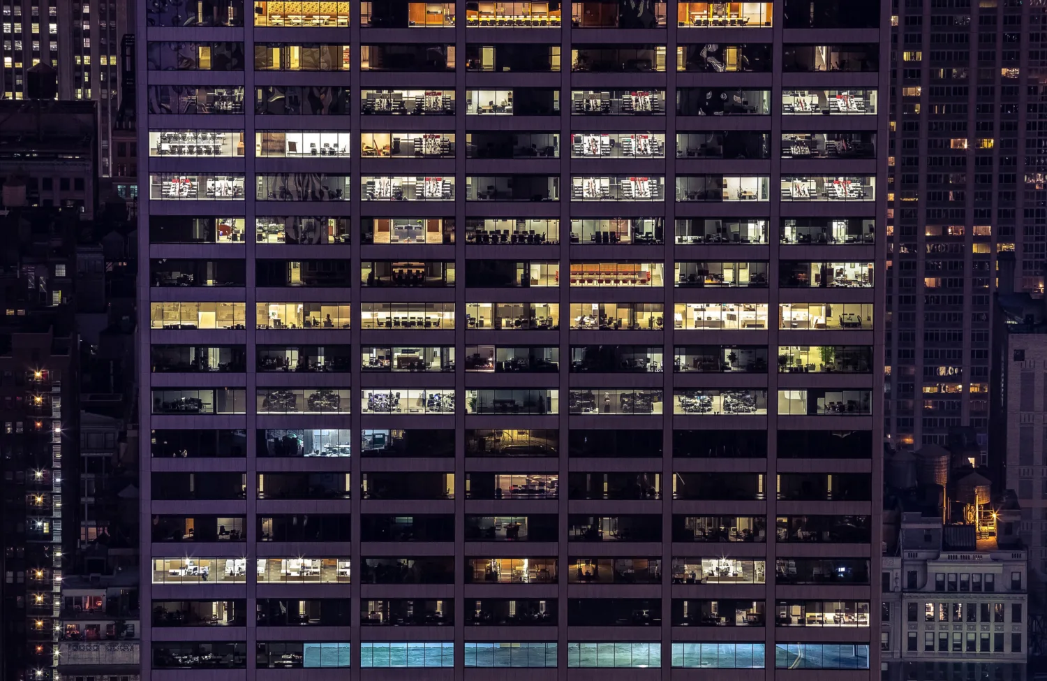 Exterior of an offlice building at night time with lit office spaces and workers
