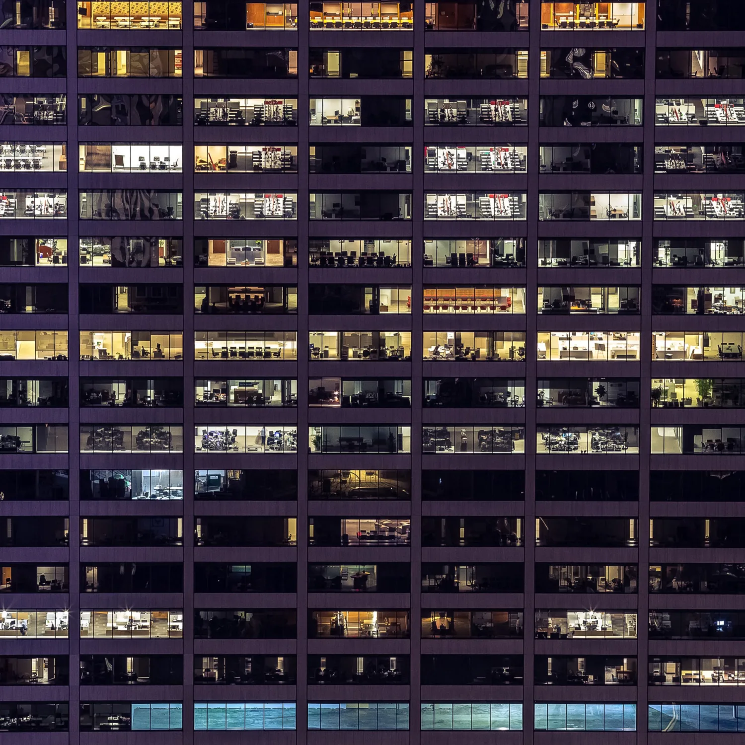 Exterior of an offlice building at night time with lit office spaces and workers