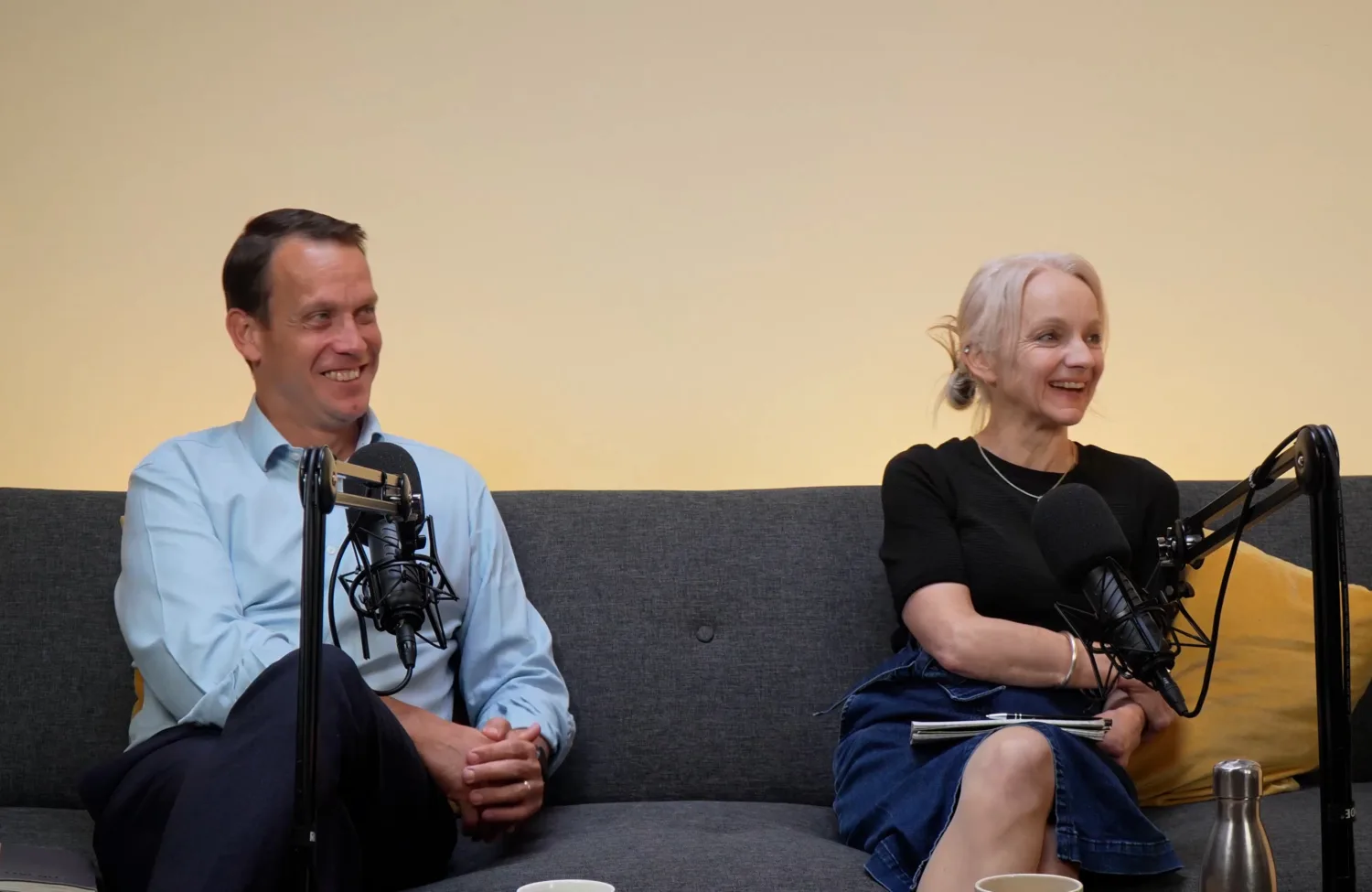 Robin and anna sat on a sofa with podcast mics