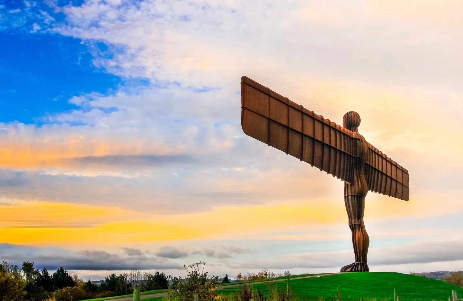 Angel of the North on a hill with a blue and yellow lit sky