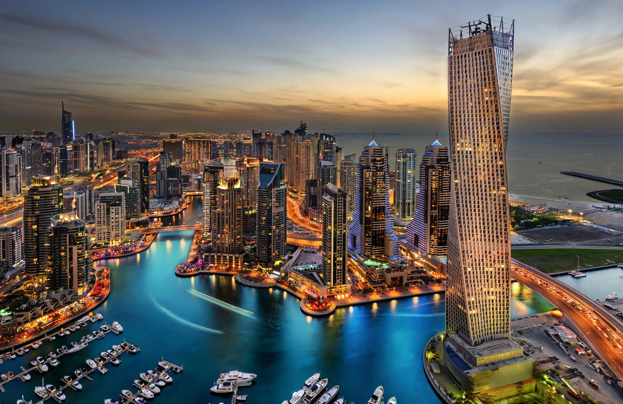 Boats in Dubai marina with orange lit buildings against a dusk sky