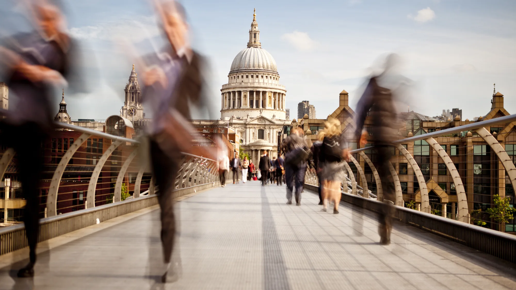 People walking across the millennium bridge with St Paul's Cathedral in the background