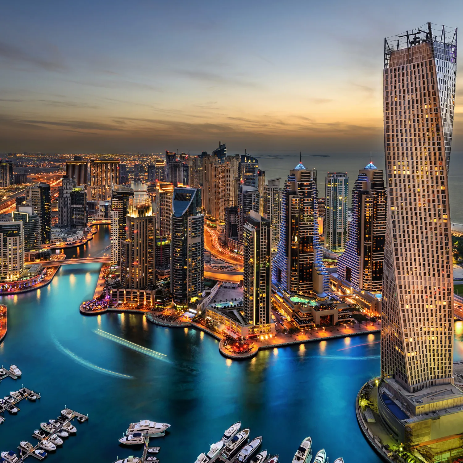 Boats in Dubai marina with orange lit buildings against a dusk sky