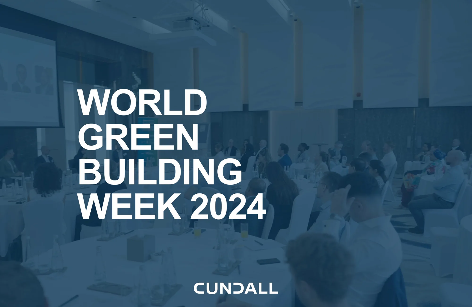 Image of an open forum with dark blue overlay and the text "World Green Building Week 2024" on top of it in all-caps.