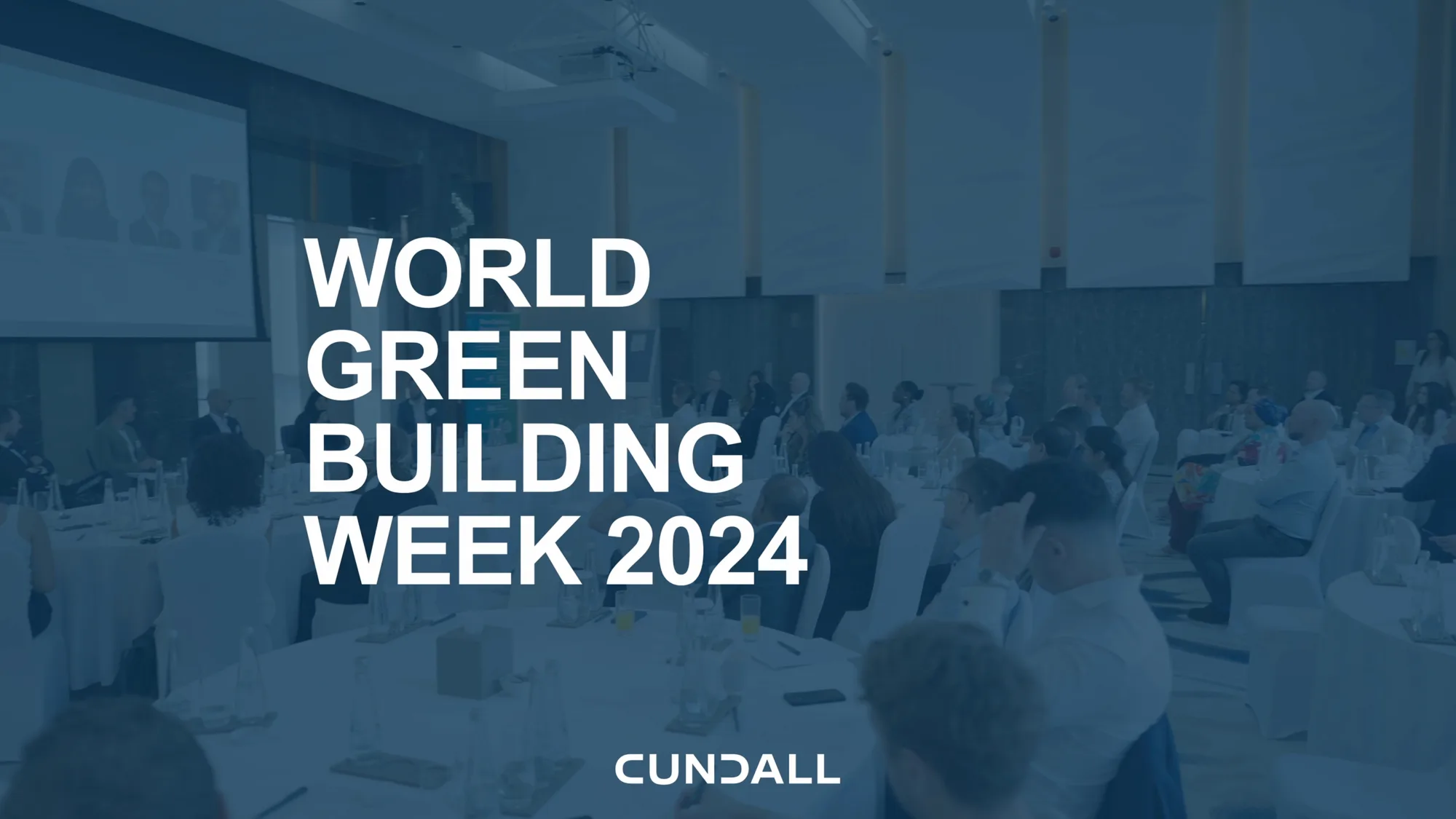 Image of an open forum with dark blue overlay and the text "World Green Building Week 2024" on top of it in all-caps.