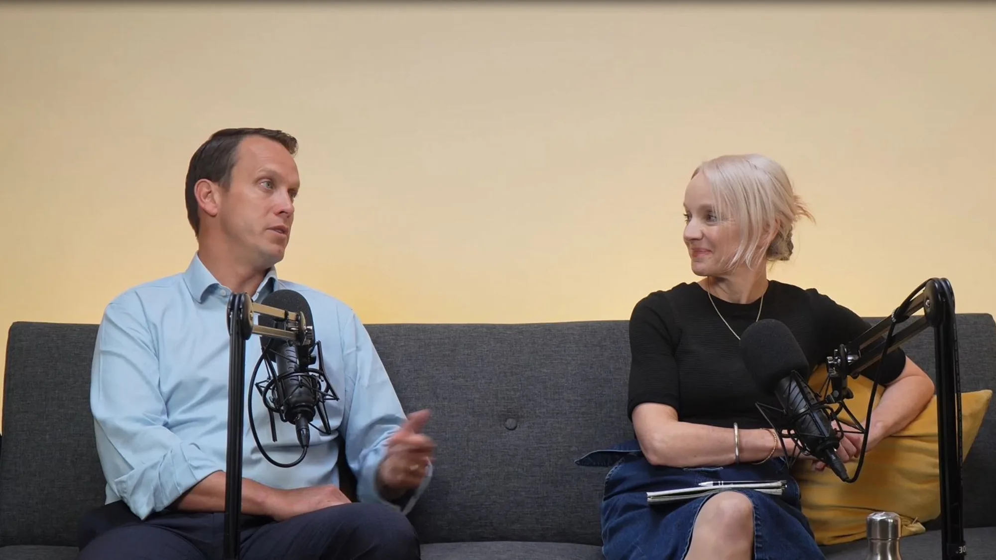 Robin Pritchett and Anna Hollyman sitting on grey sofa talking into microphones