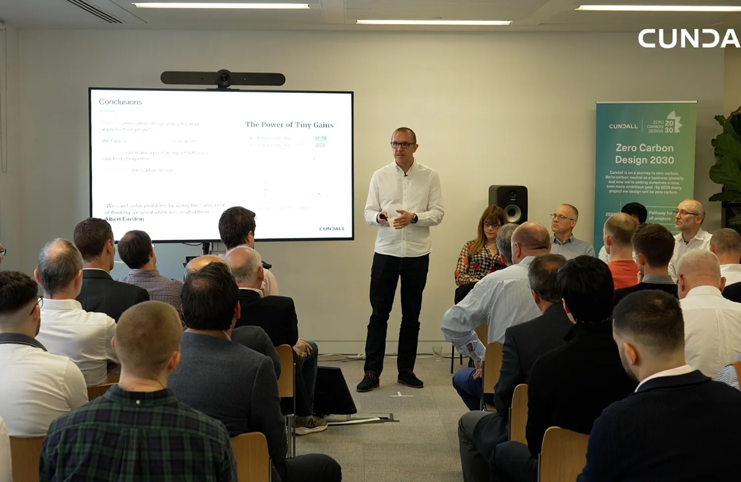 Peter Liddle presenting standing in front of the screen with room of people watching