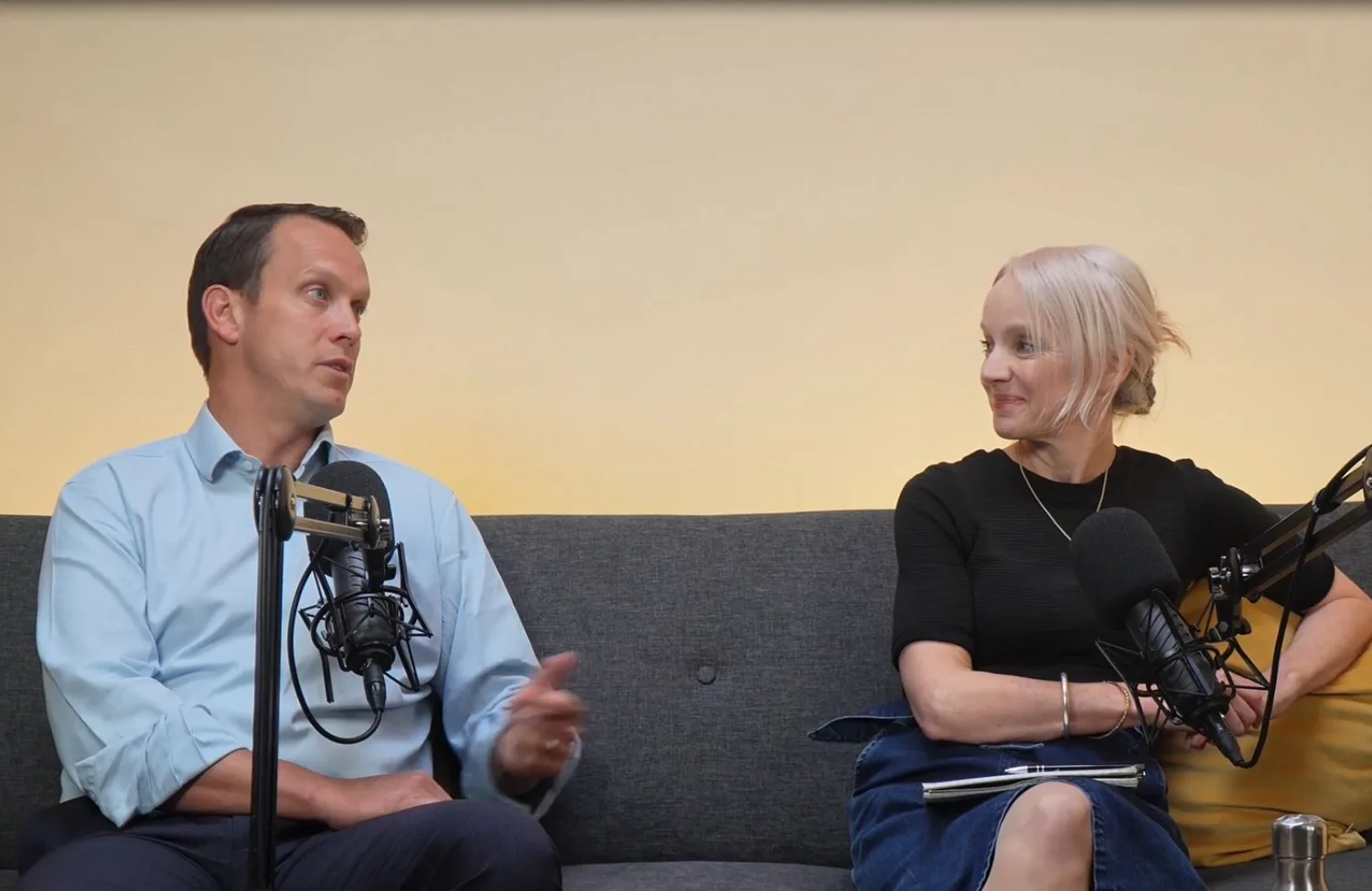 Robin Pritchett and Anna Hollyman sitting on grey sofa talking into microphones