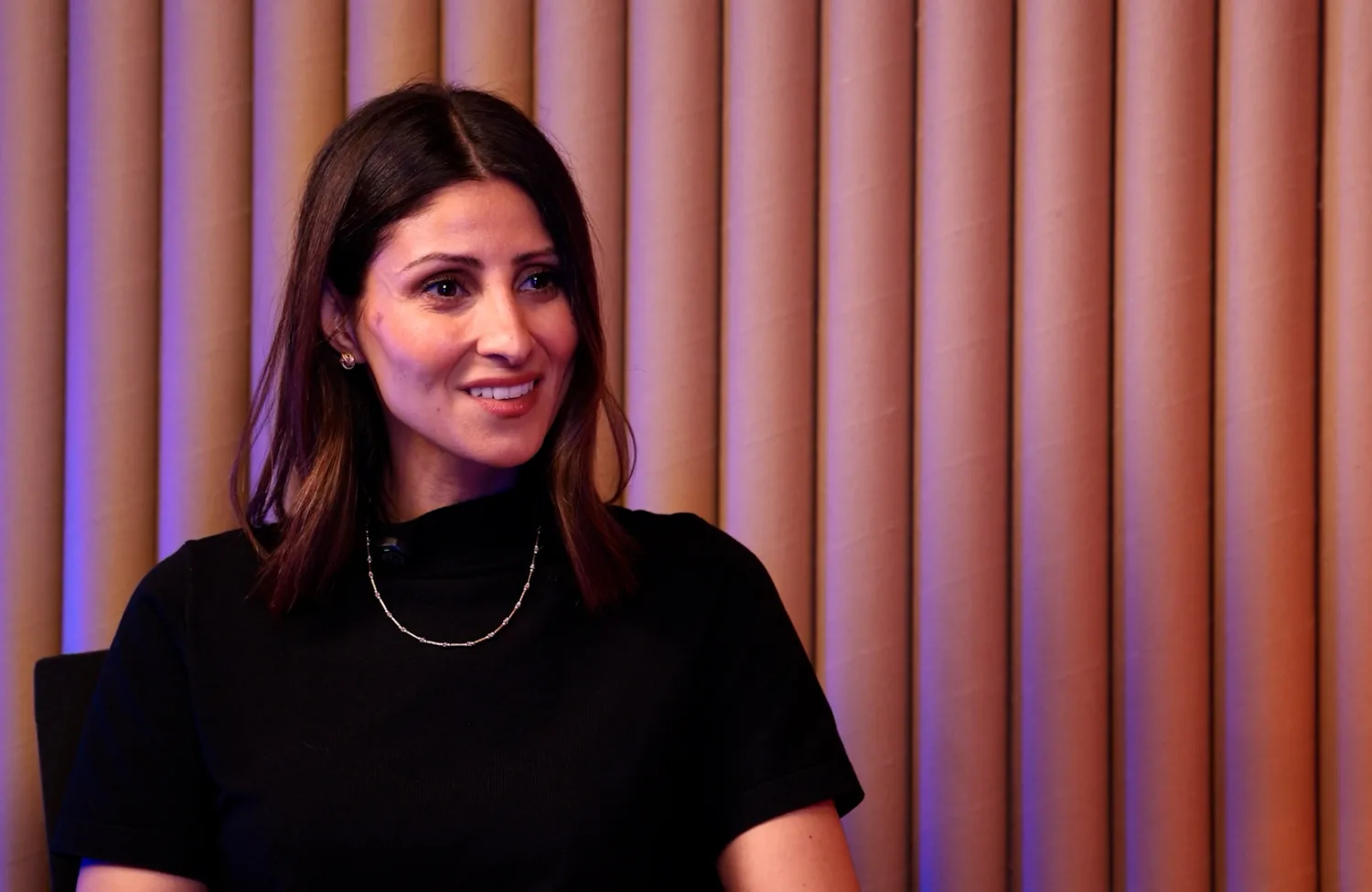 Noelle Halabi, with black long hair and black dress, being interviewed and smiling.